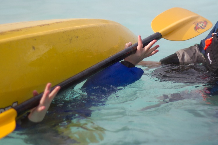 Upsidedown, underwater in kayak holding paddle above water.